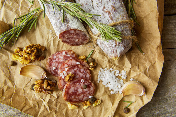 Italian salami wih sea salt, rosemary, garlic and nuts on paper. Rustic style. Close up.