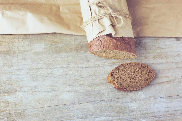 Krájený bochník chleba zabalený v papíru na dřevěném stole. — Stock fotografie