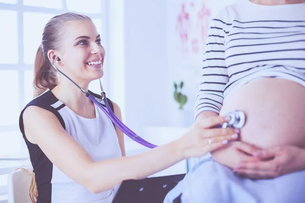 Молодая женщина-врач со стетоскопом и планшетом разговаривает с беременной женщиной в больнице. — стоковое фото