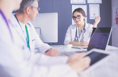 Ciddi bir tıbbi ekip parlak bir ofiste dizüstü bilgisayar kullanıyor.