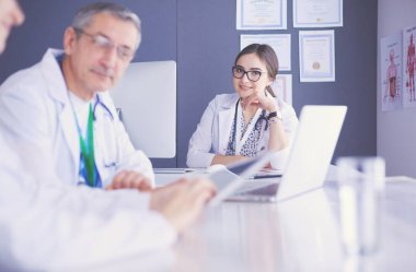 Ciddi bir tıbbi ekip parlak bir ofiste dizüstü bilgisayar kullanıyor.