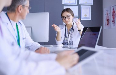 Ciddi bir tıbbi ekip parlak bir ofiste dizüstü bilgisayar kullanıyor.