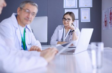 Ciddi bir tıbbi ekip parlak bir ofiste dizüstü bilgisayar kullanıyor.