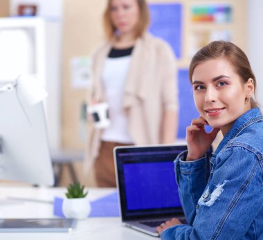 İki genç kadın masada enstrümanlar, planlar ve dizüstü bilgisayarlarla oturuyor..
