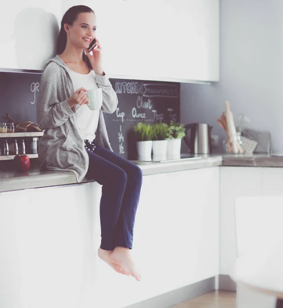 Vrouw met behulp van mobiele telefoon zitten in moderne keuken. — Stockfoto