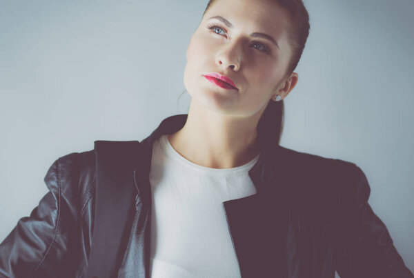 portrait of beautiful young brunette woman in stylish black jacket on gray.