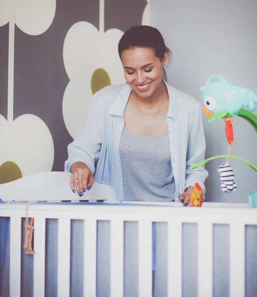 Jonge vrouw stond in de buurt van childrens kinderbed. Jonge moeder — Stockfoto