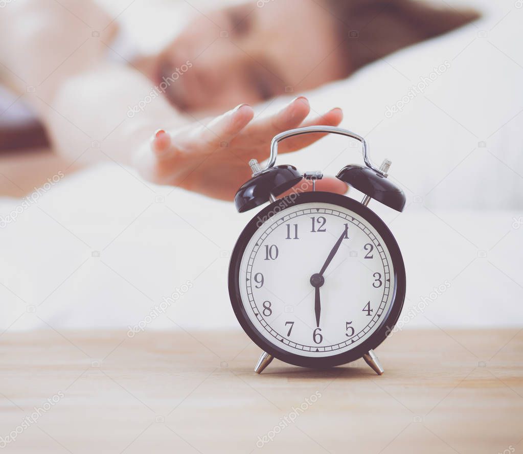 Young sleeping woman and alarm clock in bedroom at home. Young sleeping woman.