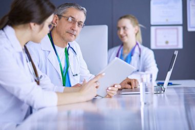 Ciddi bir tıbbi ekip parlak bir ofiste dizüstü bilgisayar kullanıyor.