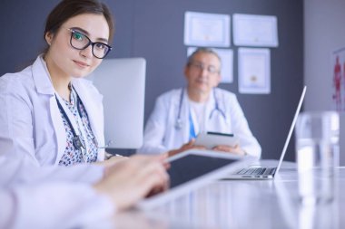 Ciddi bir tıbbi ekip parlak bir ofiste dizüstü bilgisayar kullanıyor.