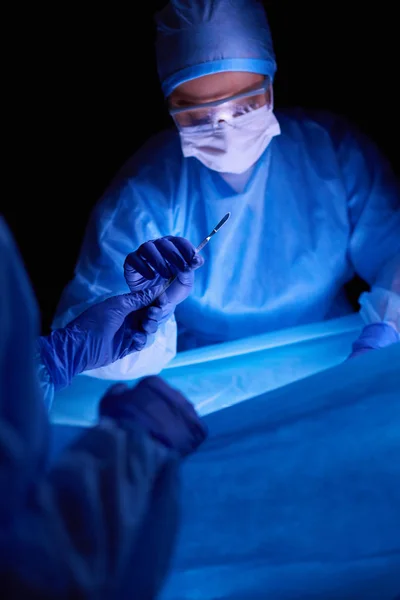 Doctor performing surgery in a dark background. — Stock Photo, Image