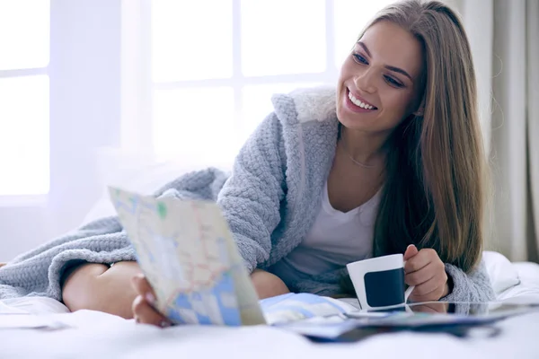 Avslappnad ung kvinna sitter på sängen med en kopp kaffe och digital tablett — Stockfoto