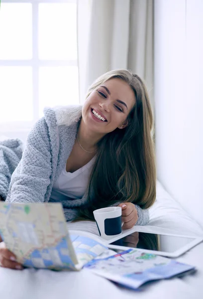 Relaxado jovem mulher sentada na cama com uma xícara de café e tablet digital — Fotografia de Stock