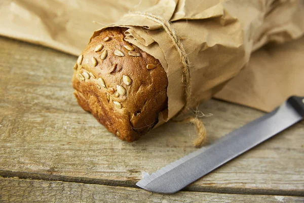 Een brood verpakt in papier op houten tafel. — Stockfoto