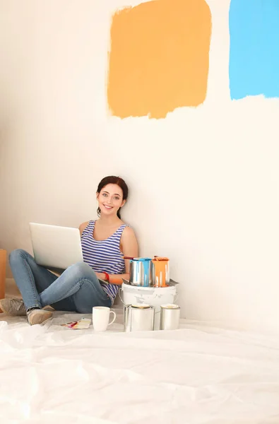 Portret van de jonge vrouw tijdens het schilderen van nieuw appartement, zitten met laptop. Jonge vrouw met laptop — Stockfoto