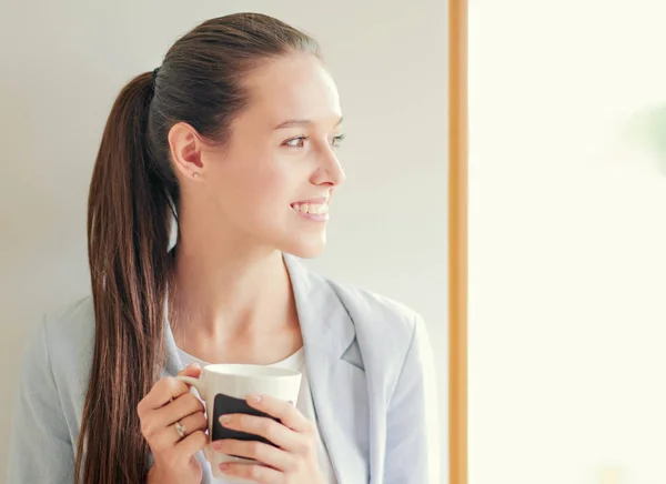 Attractive woman sitting at desk in office having takeaway coffee. — Stock Photo, Image