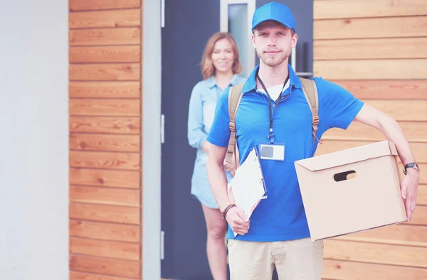 Lächelnder Zusteller in blauer Uniform liefert Paketkasten an Empfänger aus - Kurierdienst-Konzept. Lächelnder Zusteller in blauer Uniform — Stockfoto