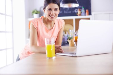 Mutfakta dizüstü bilgisayara benzeyen tariflerle gülümseyen genç bir kadın. Gıda blogcusu kavramı.