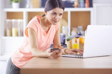 Mutfakta dizüstü bilgisayara benzeyen tariflerle gülümseyen genç bir kadın. Gıda blogcusu kavramı.