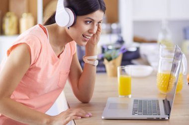 Mutfakta dizüstü bilgisayara benzeyen tariflerle gülümseyen genç bir kadın. Gıda blogcusu kavramı.