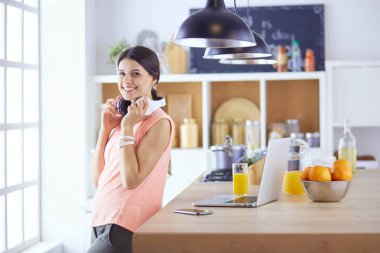 Mutfakta dizüstü bilgisayara benzeyen tariflerle gülümseyen genç bir kadın. Gıda blogcusu kavramı.