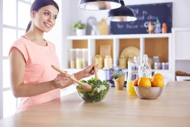 Gülümseyen genç kadın mutfakta taze salata karıştırıyor..