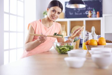 Gülümseyen genç kadın mutfakta taze salata karıştırıyor..