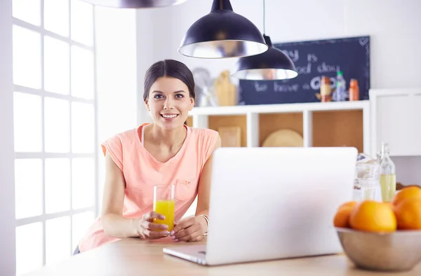 Jonge vrouw in de keuken met laptop computer uitziende recepten, glimlachen. Concept van de voedingsblogger. — Stockfoto