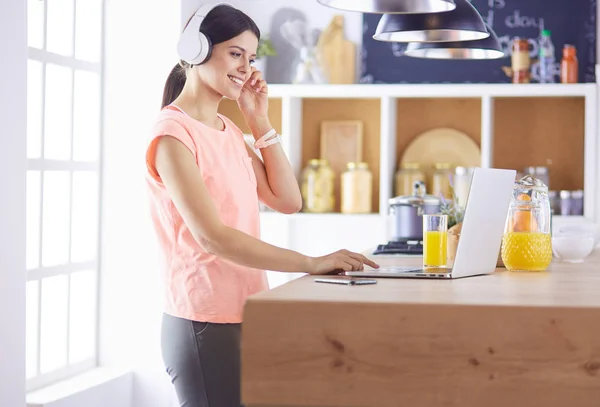 Mujer joven en la cocina con computadora portátil buscando recetas, sonriendo. Concepto de bloguero de alimentos. —  Fotos de Stock