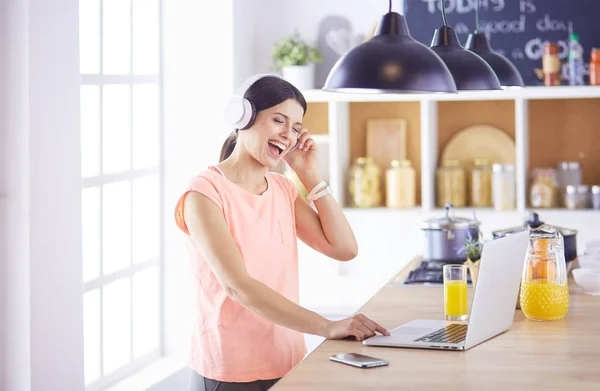 Mujer joven en la cocina con computadora portátil buscando recetas, sonriendo. Concepto de bloguero de alimentos. — Foto de Stock