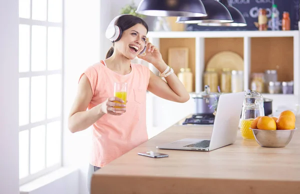 Mujer joven en la cocina con computadora portátil buscando recetas, sonriendo. Concepto de bloguero de alimentos. — Foto de Stock