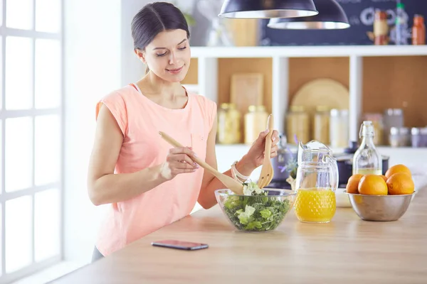 Mujer joven sonriente mezclando ensalada fresca en la cocina. — Foto de Stock