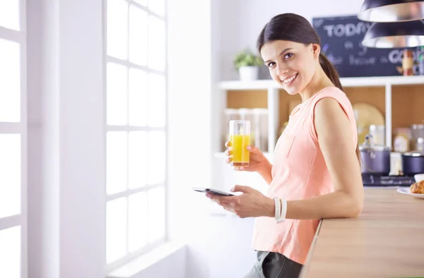 Cep telefonu görünümlü ve cam portakal suyu bir mutfakta Kahvaltı yaparken tutan gülümseyen güzel kadın. — Stok fotoğraf