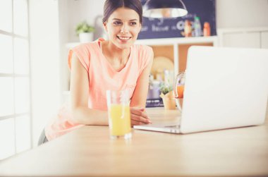 Mutfakta dizüstü bilgisayara benzeyen tariflerle gülümseyen genç bir kadın. Gıda blogcusu kavramı.