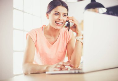 Telefondaki güzel kadın evde, mutfakta dizüstü bilgisayar kullanıyor..