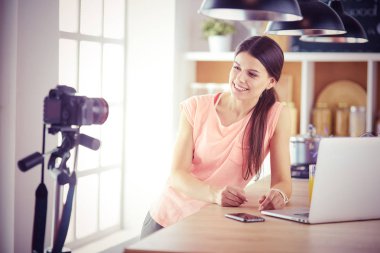 Mutfakta dizüstü bilgisayara benzeyen tariflerle gülümseyen genç bir kadın. Gıda blogcusu kavramı.