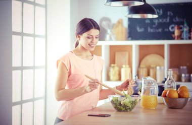 Gülümseyen genç kadın mutfakta taze salata karıştırıyor..