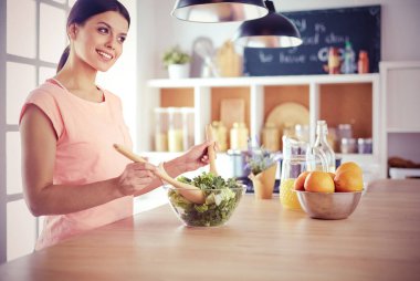 Gülümseyen genç kadın mutfakta taze salata karıştırıyor..