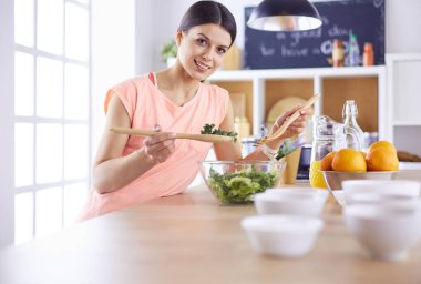 Gülümseyen genç kadın mutfakta taze salata karıştırıyor..
