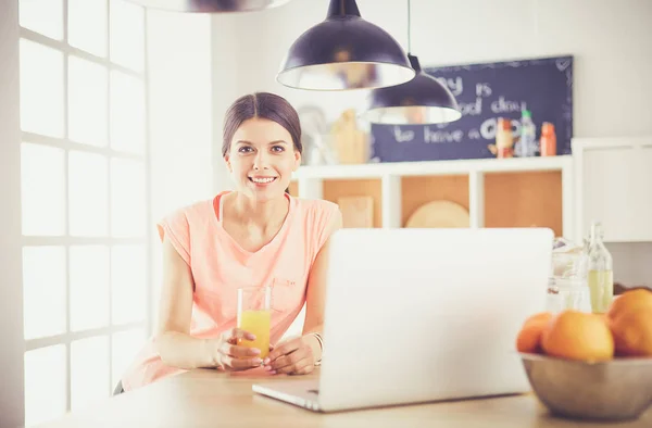 Ung kvinna i köket med bärbar dator ser recept, leende. Begreppet livsmedelsbloggare. — Stockfoto