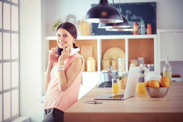 Jovem mulher na cozinha com computador portátil procurando receitas, sorrindo. Conceito de blogueiro de alimentos. — Fotografia de Stock