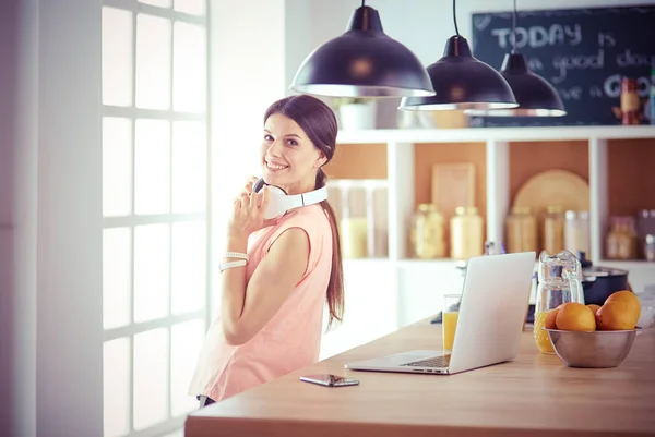 Mujer joven en la cocina con computadora portátil buscando recetas, sonriendo. Concepto de bloguero de alimentos. — Foto de Stock