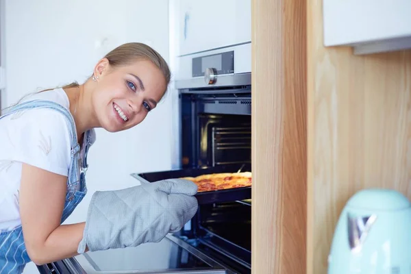 Šťastná mladá žena vaří pizzu doma — Stock fotografie