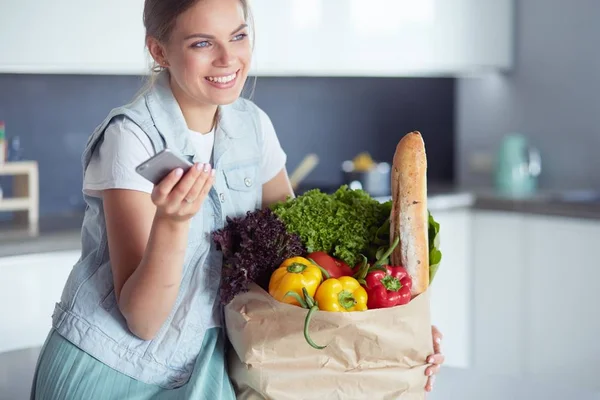 Ung kvinna som håller i matkassen med grönsaker.Står i köket — Stockfoto