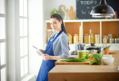 Mutfakta yemek yapmak için tablet bilgisayar kullanan genç bir kadın.