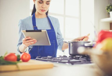Mutfakta yemek yapmak için tablet bilgisayar kullanan genç bir kadın.