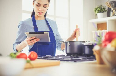 Mutfakta yemek yapmak için tablet bilgisayar kullanan genç bir kadın.