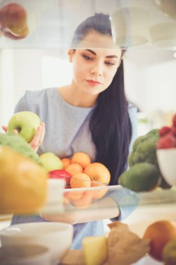 Gülümseyen kadın buzdolabından taze meyve alıyor, sağlıklı yiyecek konsepti.