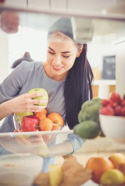 Gülümseyen kadın buzdolabından taze meyve alıyor, sağlıklı yiyecek konsepti.