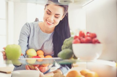 Gülümseyen kadın buzdolabından taze meyve alıyor, sağlıklı yiyecek konsepti.
